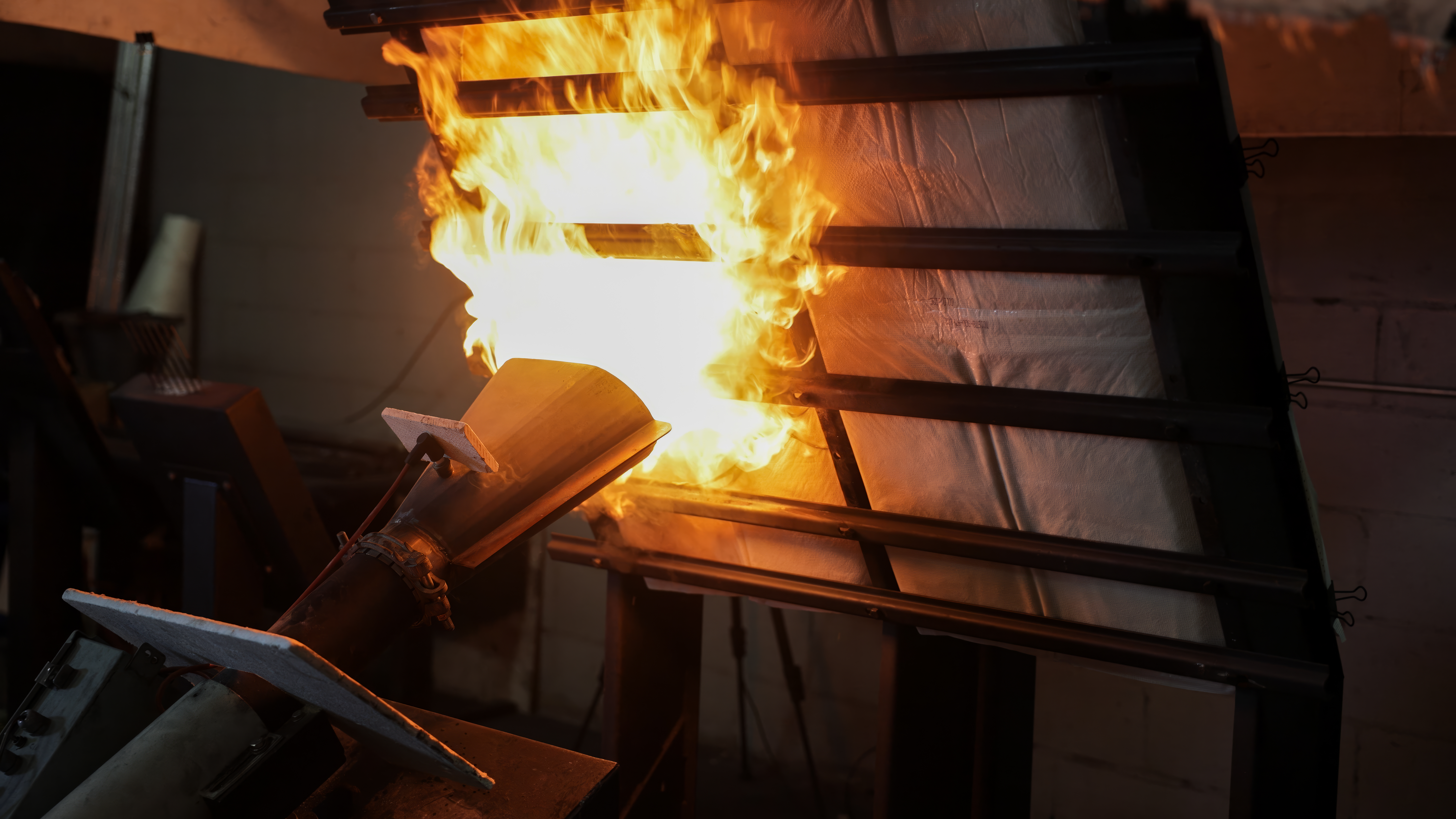 Intense industrial fire test, where a powerful flame is directed at a wall or panel structure to evaluate its fire resistance and performance under extreme heat.