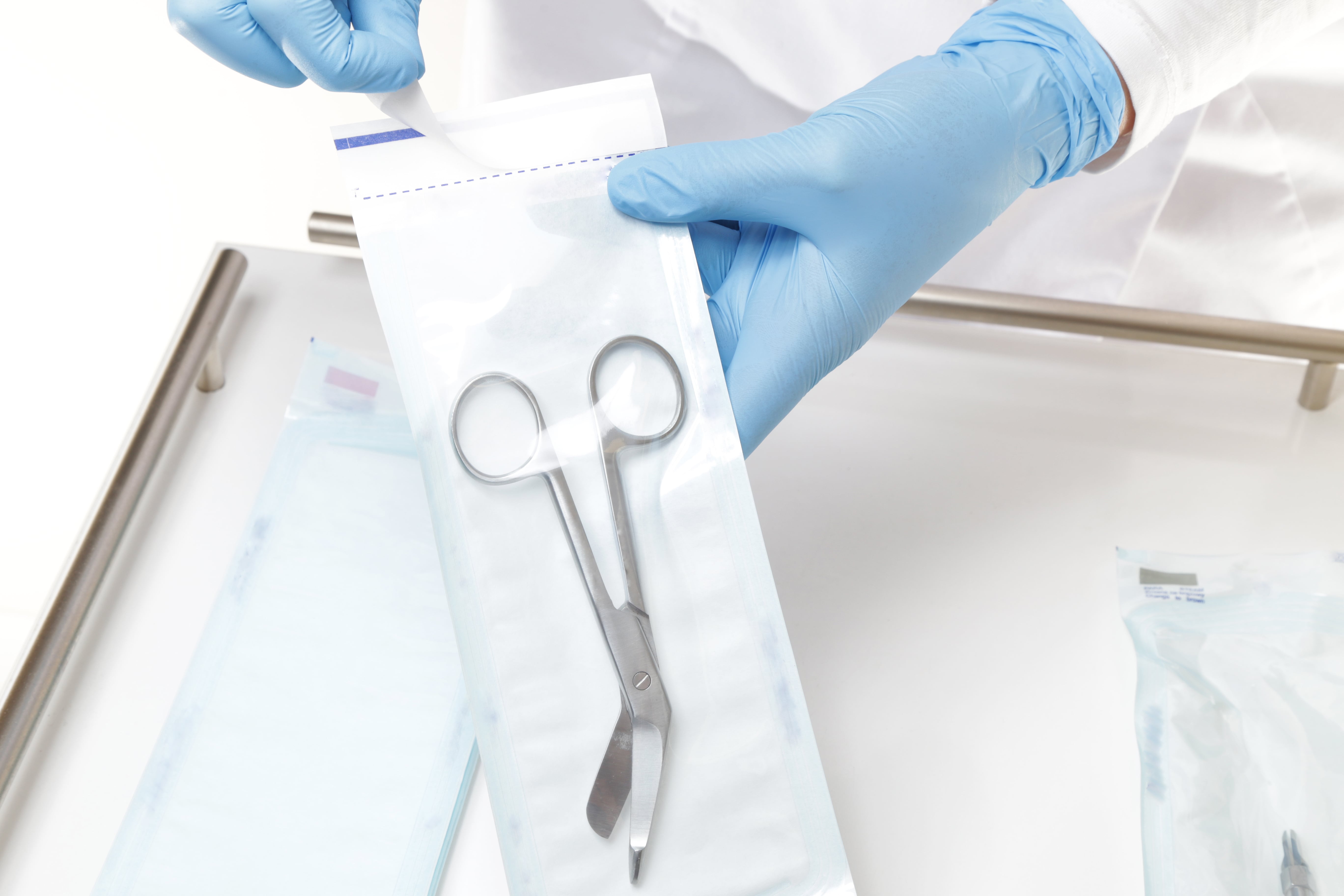 Dispositif médical stérilisé dans un emballage transparent, manipulé par une personne portant des gants bleus.