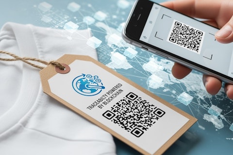 A hand using a smartphone to scan a QR code on a clothing tag labelled “TRACEABILITY POWERED BY BLOCKCHAIN,” illustrating digital product tracking.