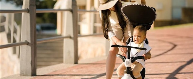 Une mère aidant son enfant à utiliser un tricycle sur une promenade ensoleillée.