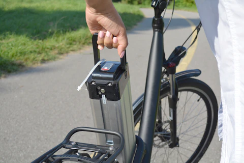 Woman holding battery pack of electric bicycle near her e bike