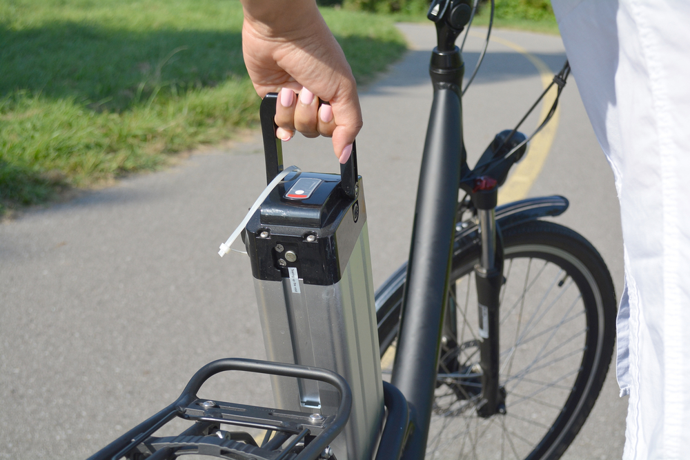 Woman holding battery pack of electric bicycle near her e bike