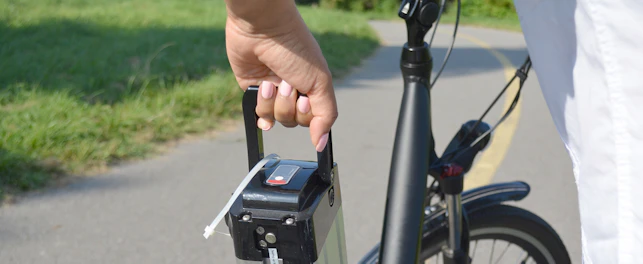 Woman holding battery pack of electric bicycle near her e bike