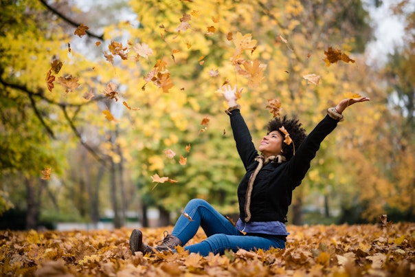 Woman sitting on top of fallen leaves on a park in autumn