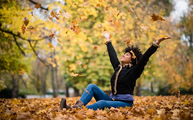 Woman sitting on top of fallen leaves on a park in autumn