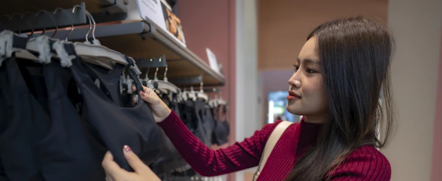 Young asian woman choosing black sports bra from a clothing rack in a store