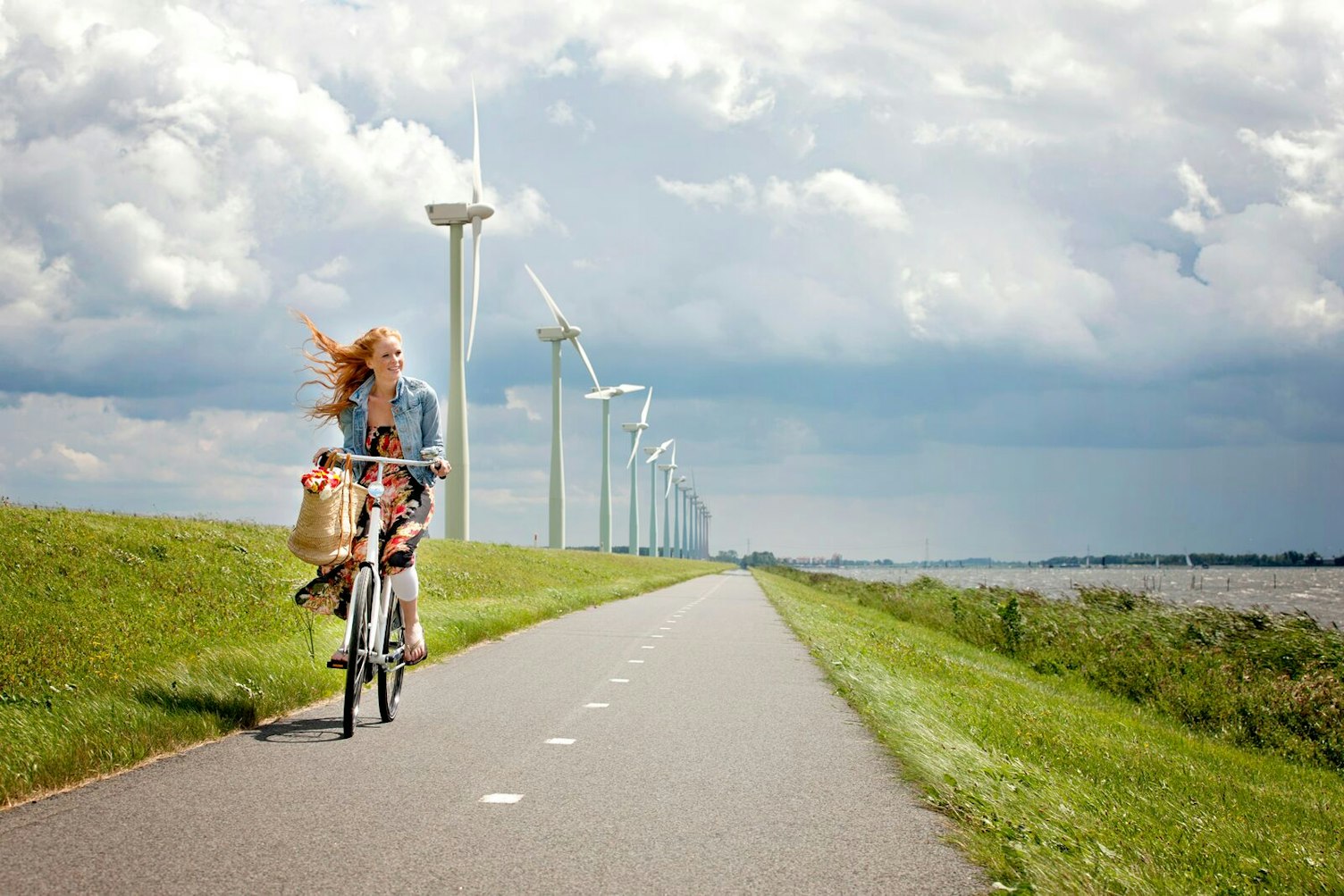 Young Woman Cycling on a Road Passing a Wind Farm