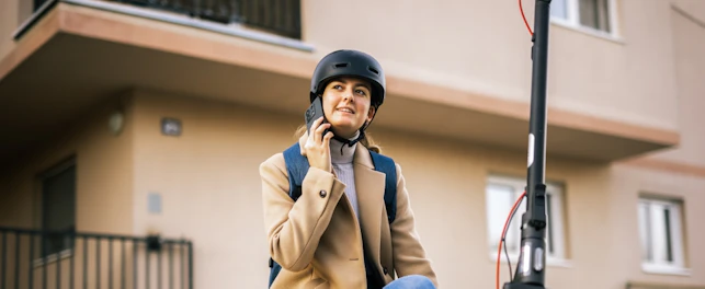 Young Woman Riding an Electric Scooter in the City Wearing a Helmet and Talking on her Smart Phone