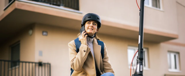 Young Woman Riding an Electric Scooter in the City Wearing a Helmet and Talking on her Smart Phone
