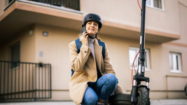 Young Woman Riding an Electric Scooter in the City Wearing a Helmet and Talking on her Smart Phone