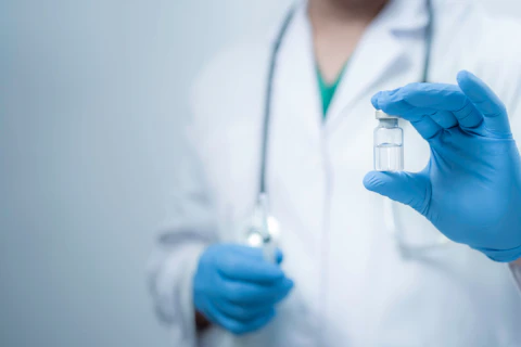 A medical worker wearing a white coat is holding a vaccine bottle