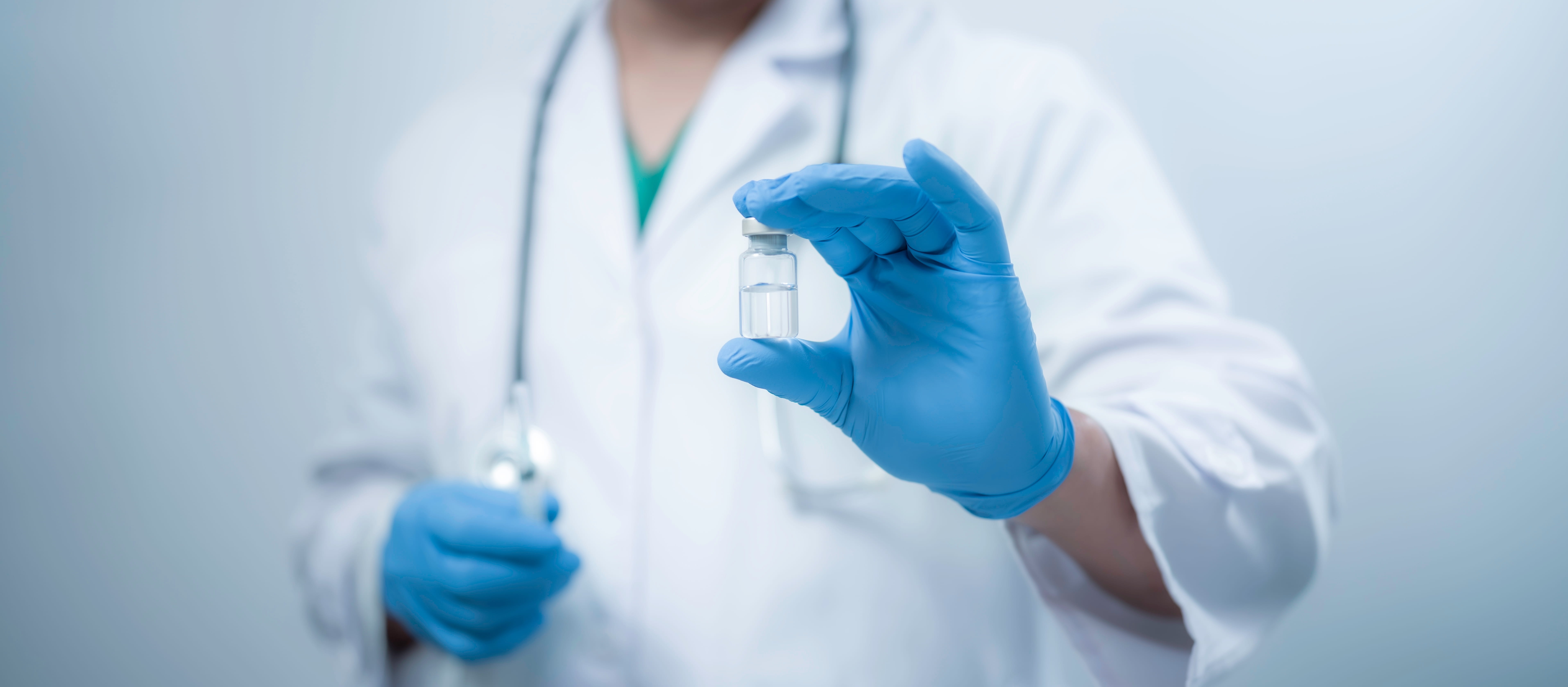 A medical worker wearing a white coat is holding a vaccine bottle
