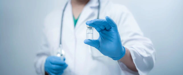 A medical worker wearing a white coat is holding a vaccine bottle