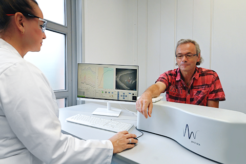 A healthcare professional operating a Confocal Raman Microspectroscopy (CRM) while a patient rests their arm on the machine