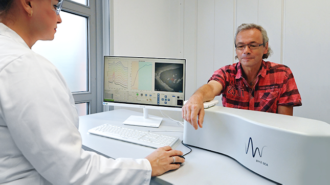 A healthcare professional operating a Confocal Raman Microspectroscopy (CRM) while a patient rests their arm on the machine