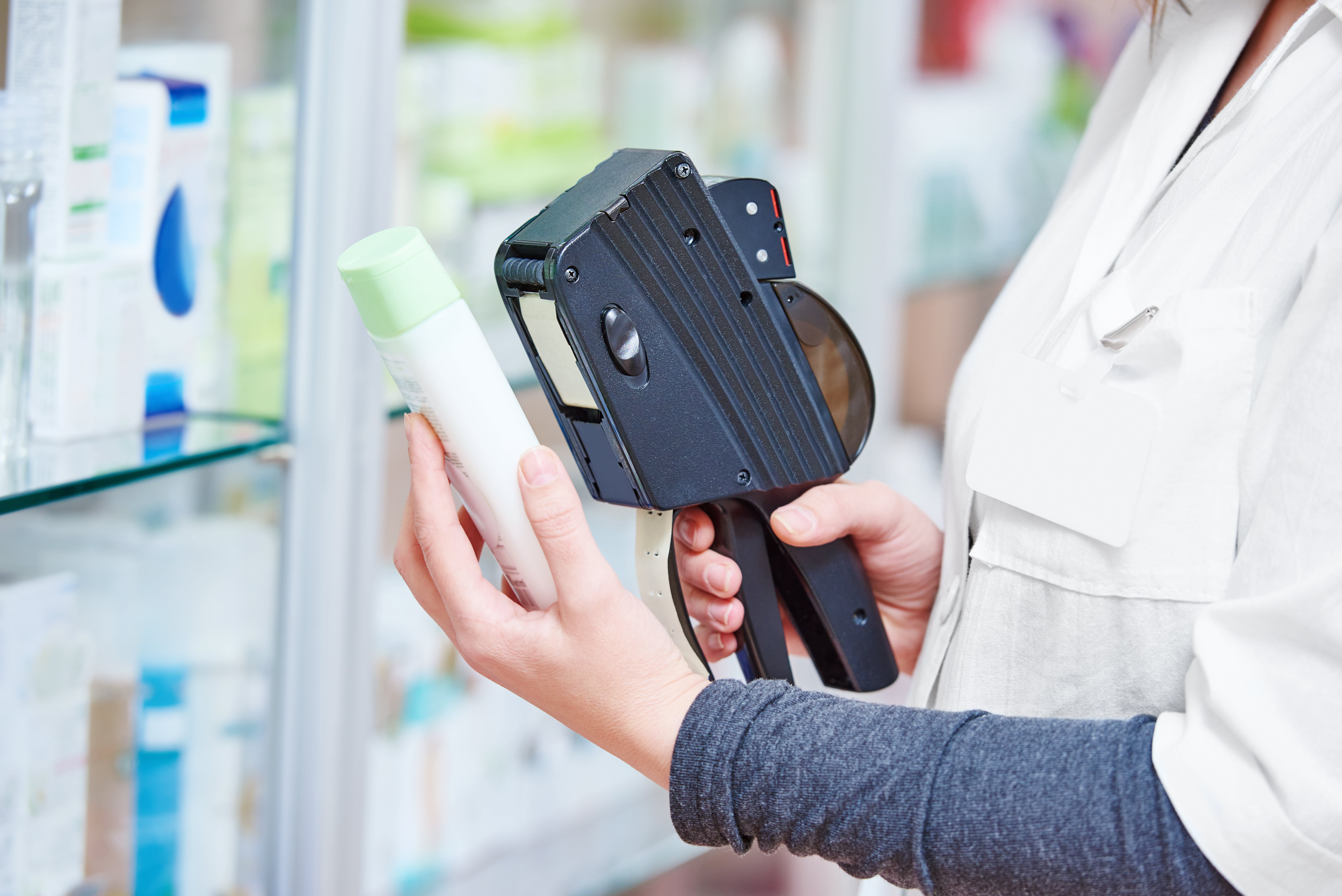 Hand van vrouwelijke apotheker die een etiketteerpistool gebruikt om een prijskaartje van een geneesmiddel in de drogisterij te plakken