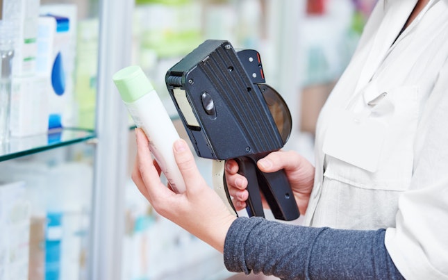 Hand van vrouwelijke apotheker die een etiketteerpistool gebruikt om een prijskaartje van een geneesmiddel in de drogisterij te plakken