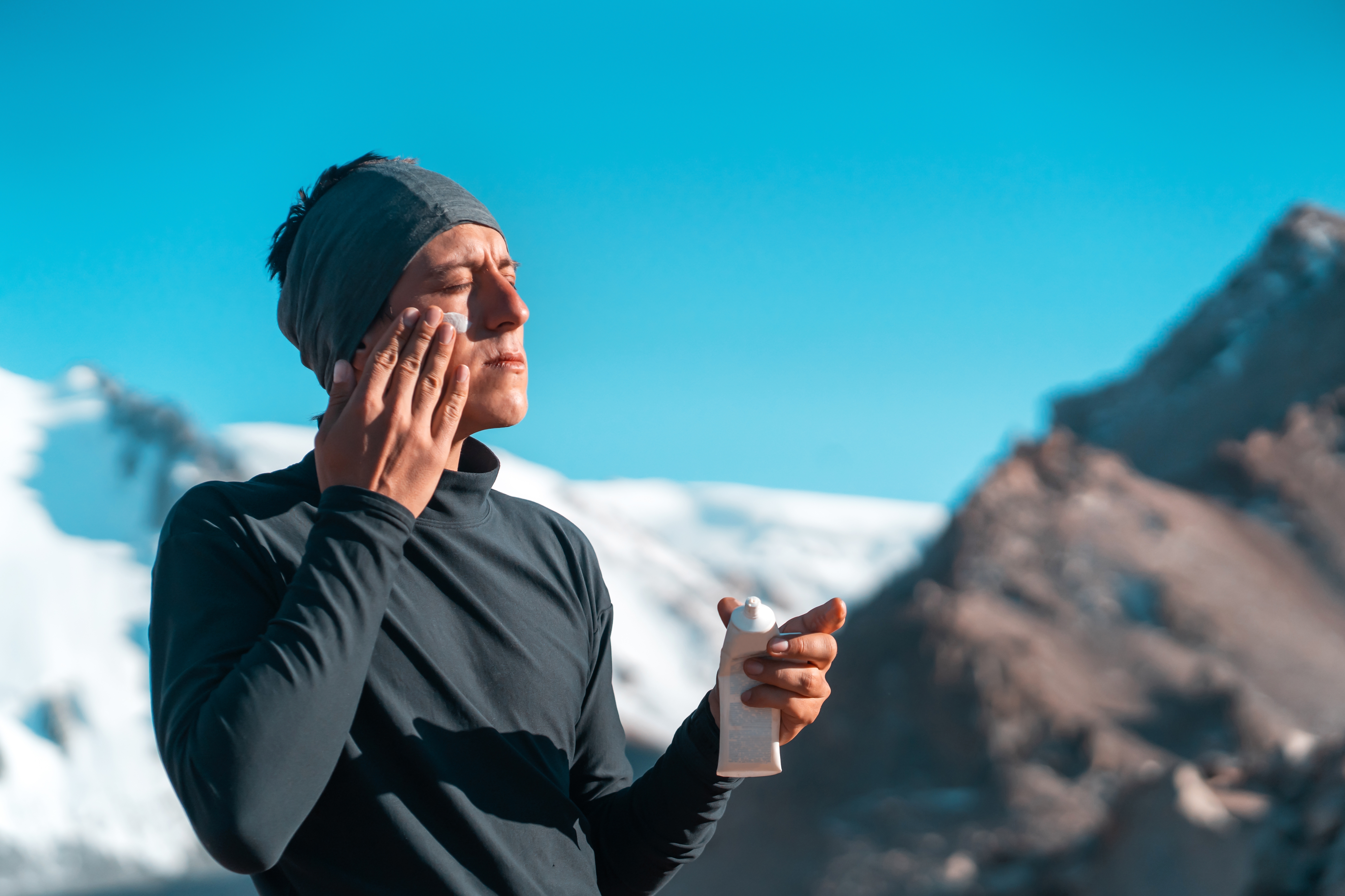 man applying sunscreen with snowy mountains
