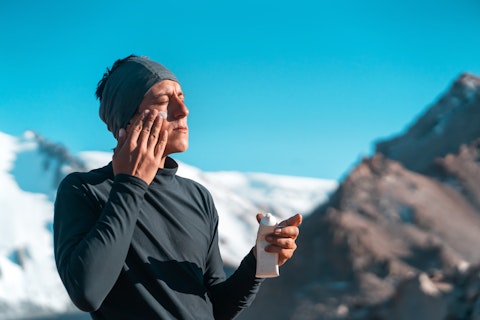 man applying sunscreen with snowy mountains