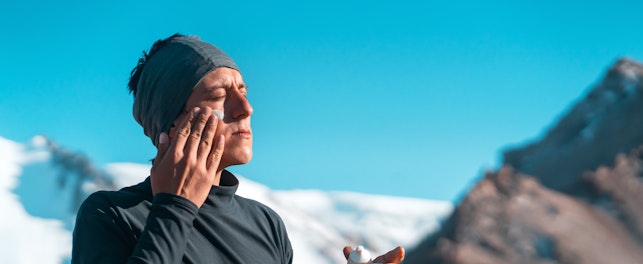 man applying sunscreen with snowy mountains