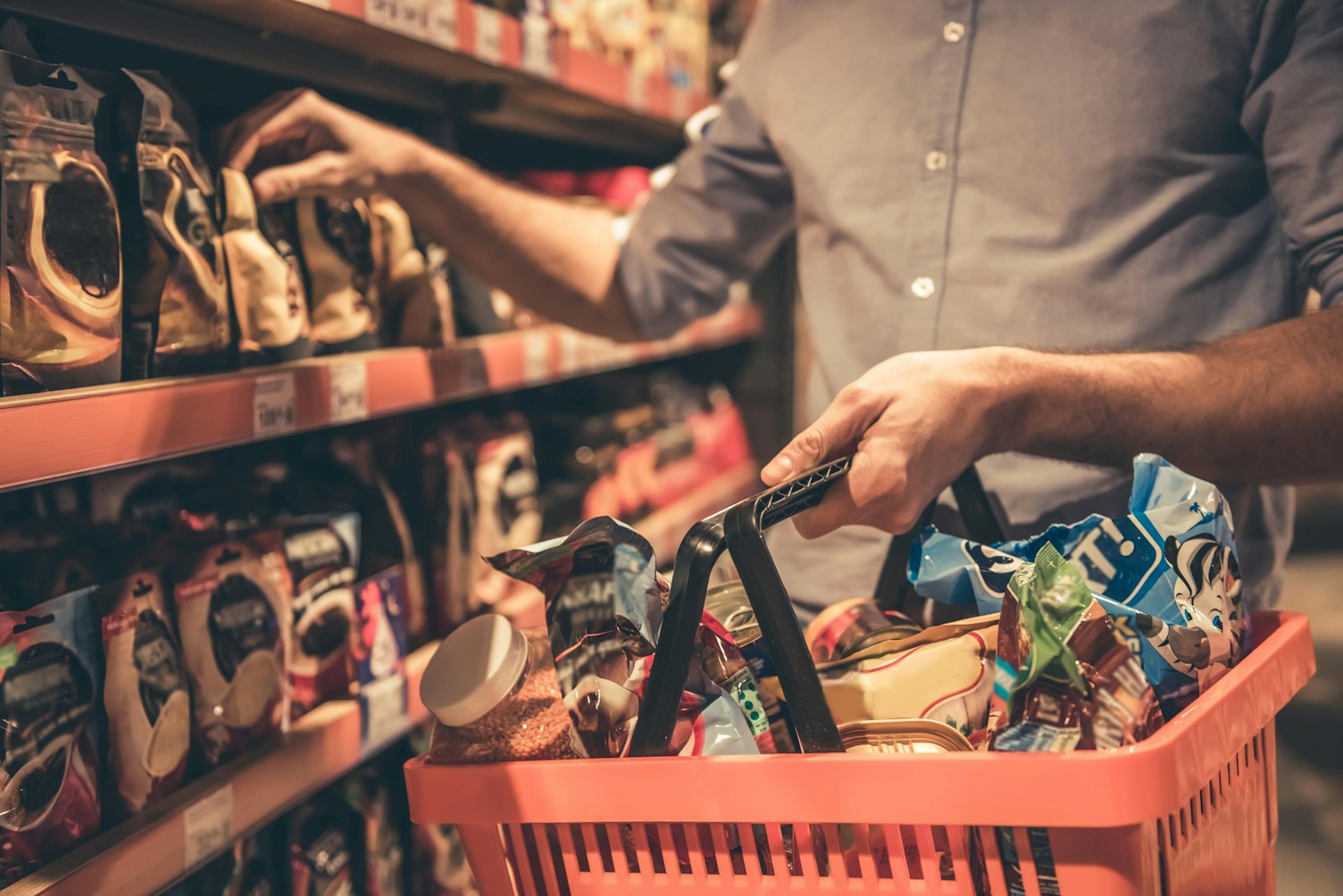 Imagen recortada de un hombre bonito con una cesta de compras haciendo compras en el supermercado