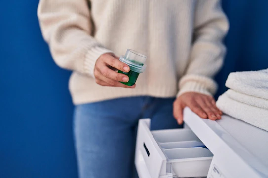 Young beautiful hispanic woman pouring detergent on washing machine at laundry room