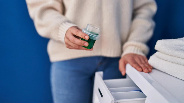 Young beautiful hispanic woman pouring detergent on washing machine at laundry room