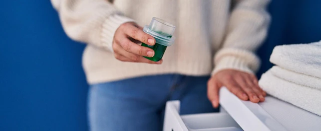 Young beautiful hispanic woman pouring detergent on washing machine at laundry room