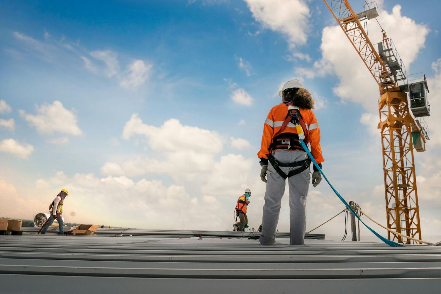 Construction worker wearing safety harness and safety line working on a metal industry roof