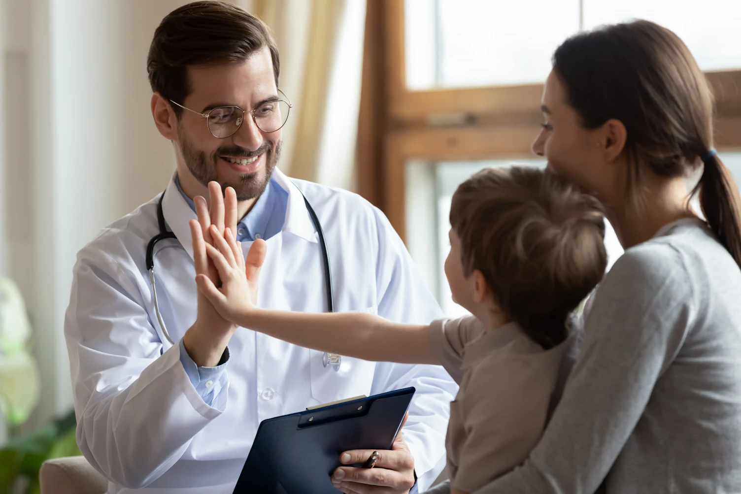 Happy playful male pediatrician give high five greeting with little boy patient