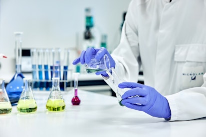 Scientifique en laboratoire effectuant une manipulation chimique avec des gants et des instruments de verrerie.