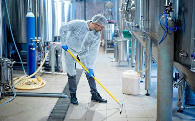 Professional Industrial Cleaner in Protective Uniform Cleaning Floor of Food Processing Plant