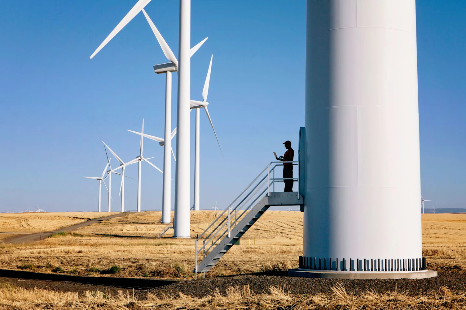 Wind farm technician standing and using a laptop at the base of a turbine