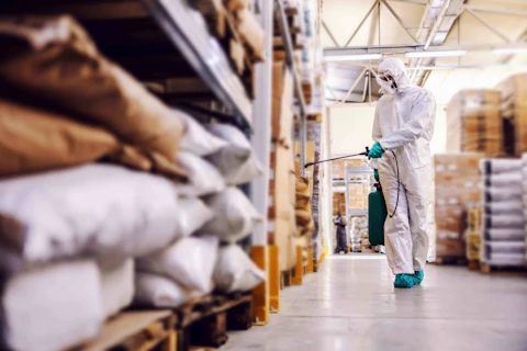 man in protective suit and mask disinfecting warehouse