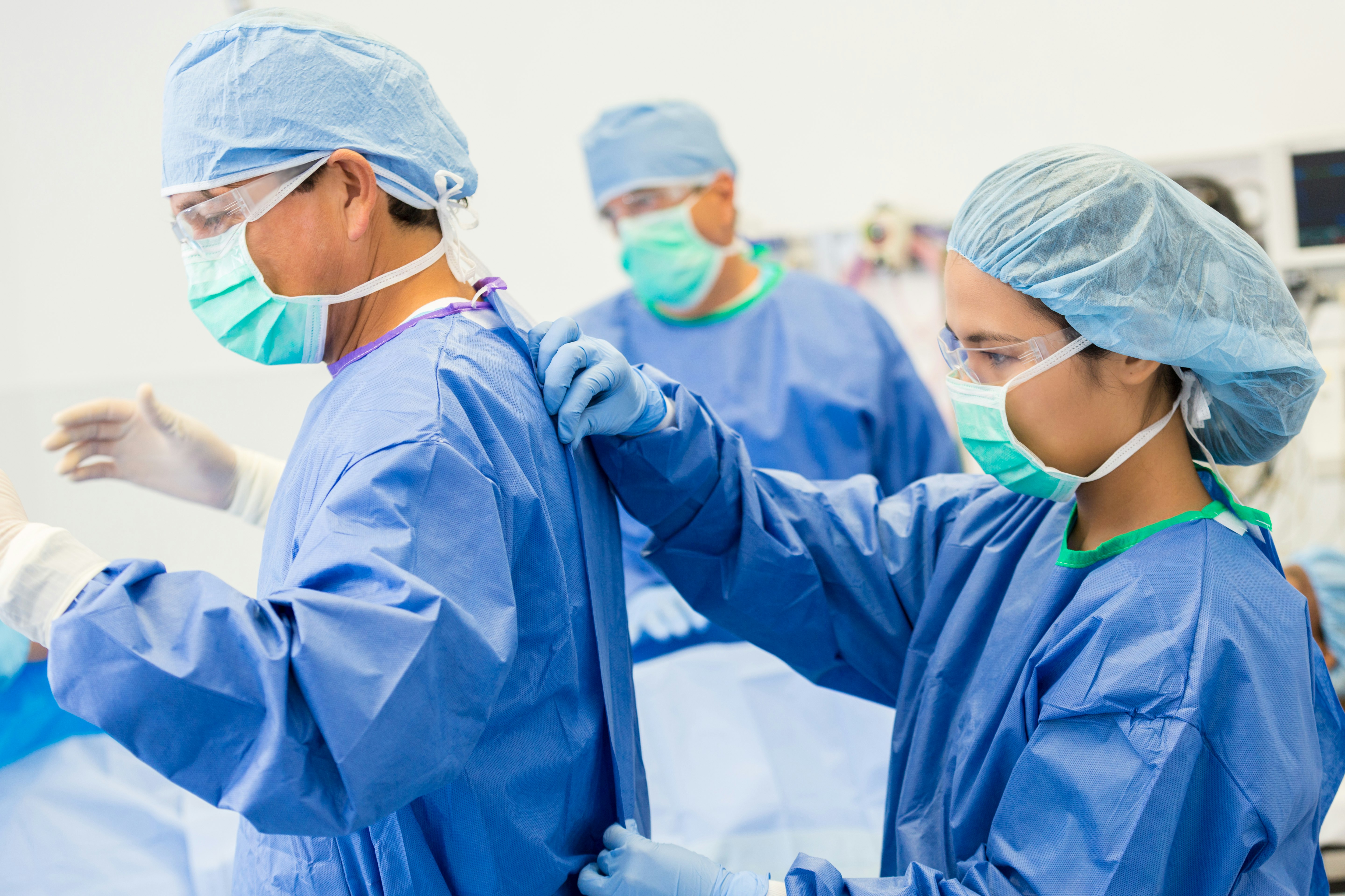 Female Surgical Technician or Nurse is Helping Lead Surgeon Put on Sterile Gown and Gloves