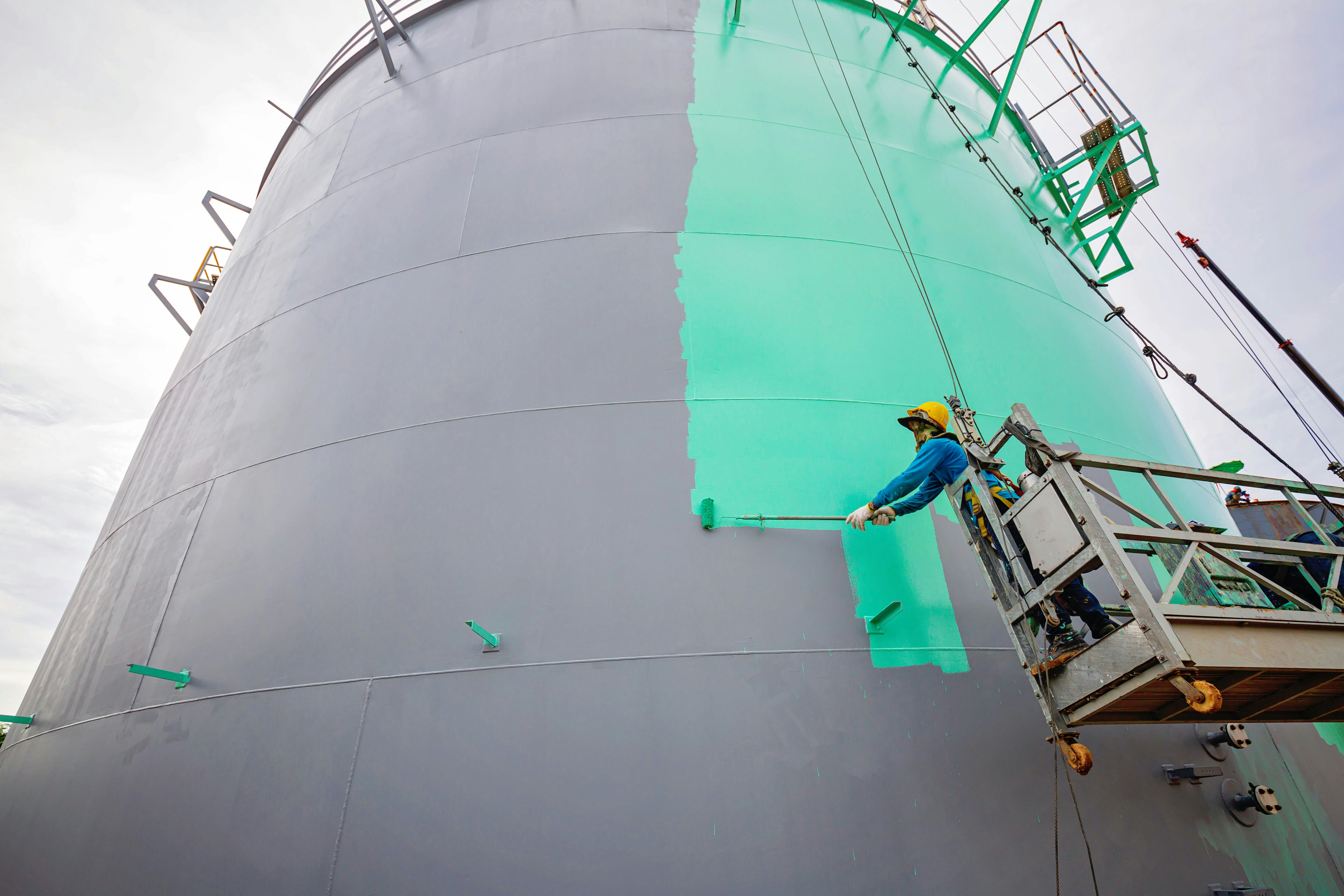 Worker Painting a Tank Oil Surface in Green