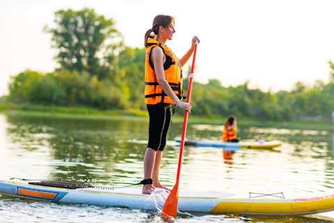 woman standing on a SUP board wearing a buoyancy aid and holding a paddle in her hand