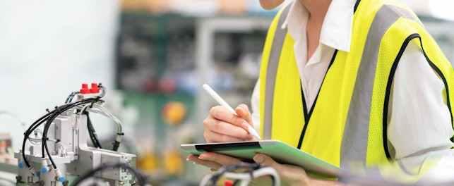 Nainen ohjaa koneiston toimintaa tabletin avulla tehtaassa