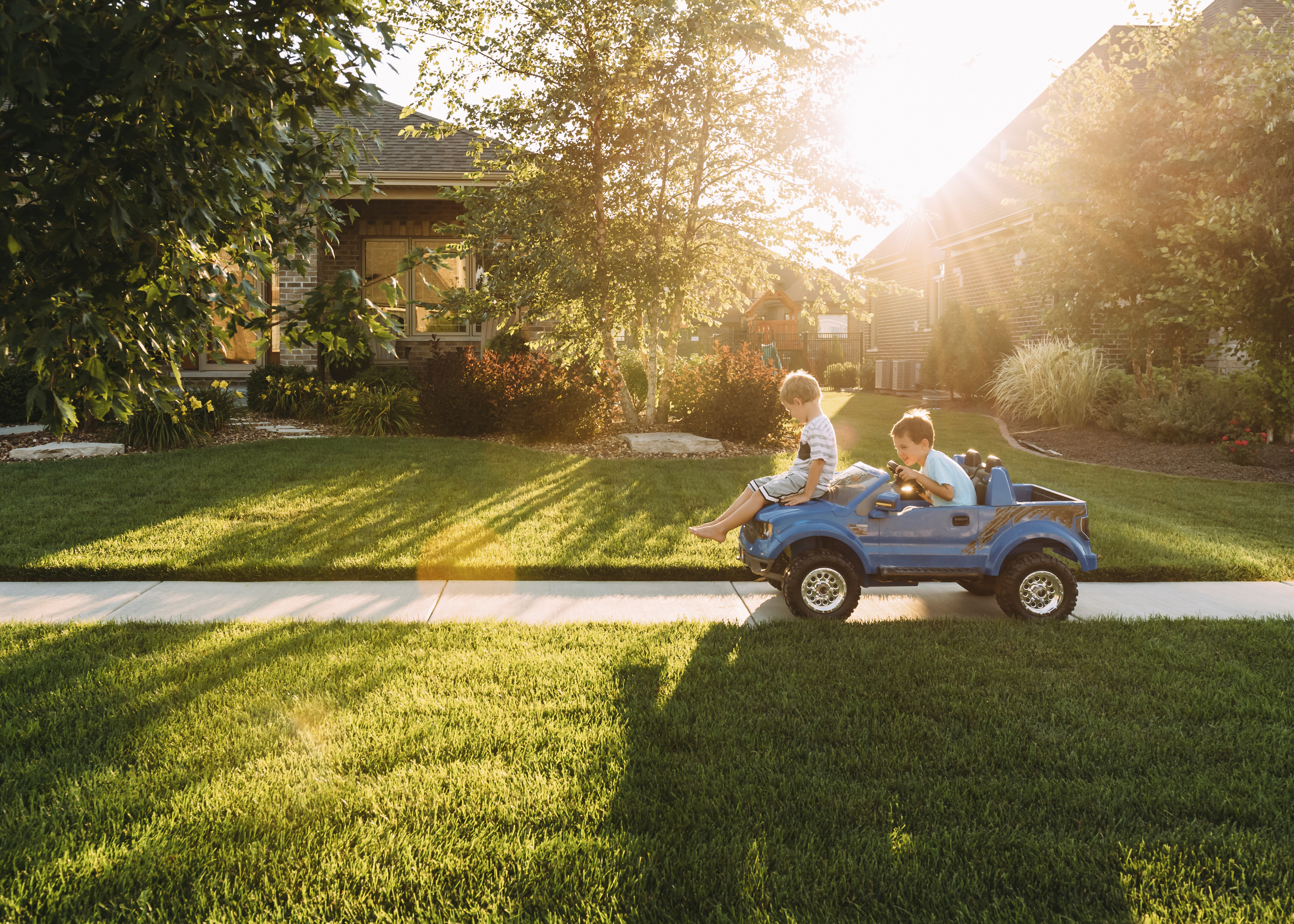 siblings playing with toy car on sidewalk at yard