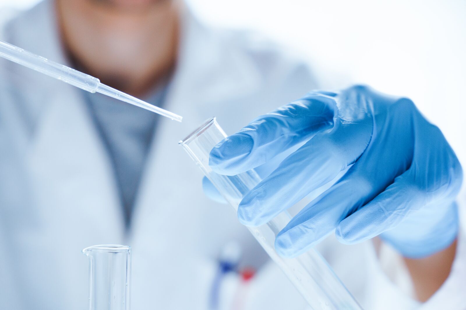 Pracownik laboratorium w rękawiczkach ochronnych przelewa badaną substancję do szklanej fiolki.