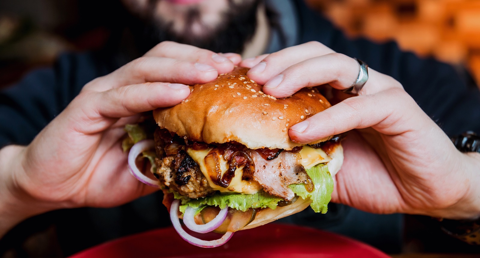 Zbliżenie na cheeseburgera trzymanego w dłoniach przez mężczyznę.