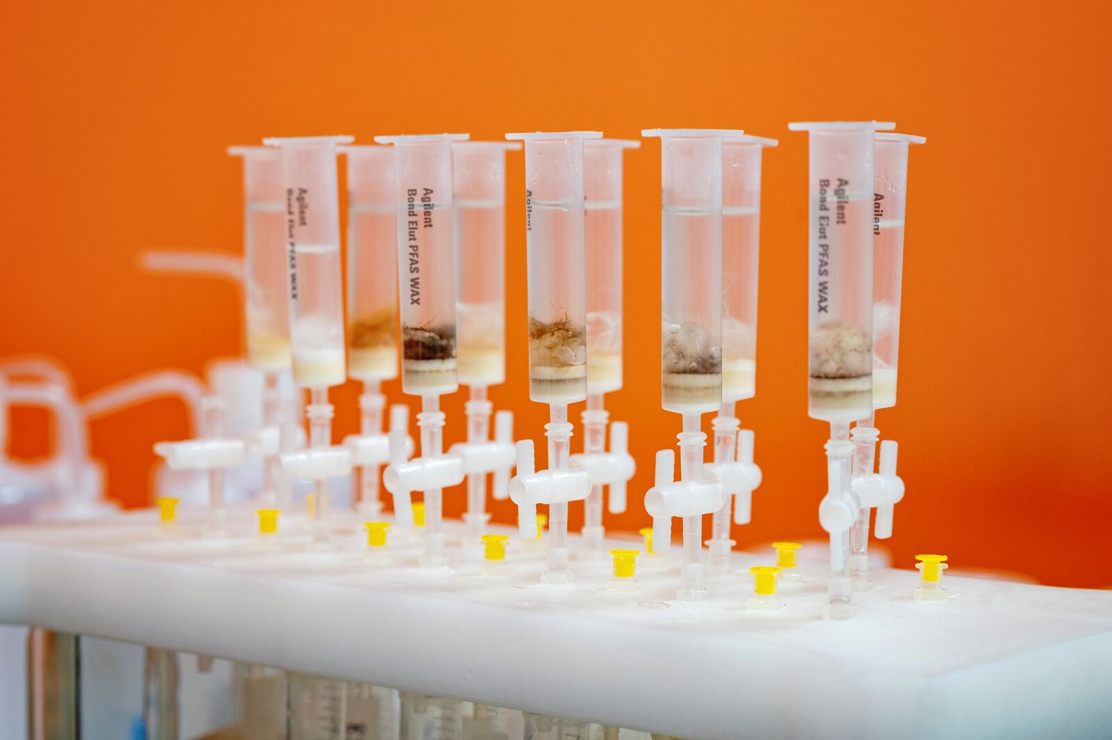 Fiolki z substancjami chemicznymi PFAS do badań w laboratorium, pomarańczowe tło.