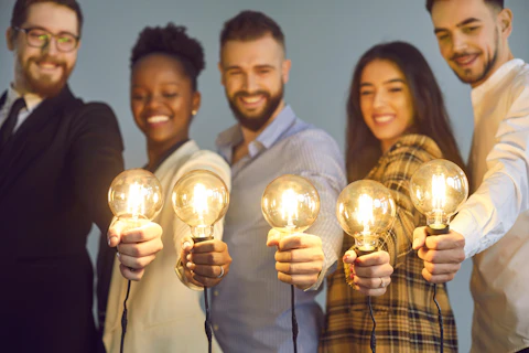 Happy creative team holding glowing lit lightbulbs. Diverse collaboration group of intelligent young multicultural business people with shining light bulbs presenting and sharing effective useful idea