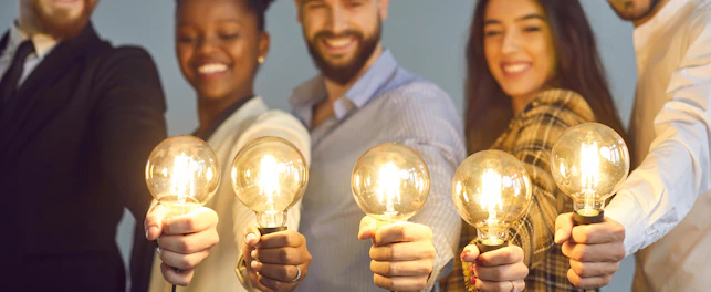 Happy creative team holding glowing lit lightbulbs. Diverse collaboration group of intelligent young multicultural business people with shining light bulbs presenting and sharing effective useful idea