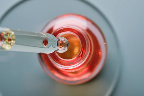 Oil or Serum bottle and pipette in petri dish on grey background. Pink cosmetic product, selective focus.