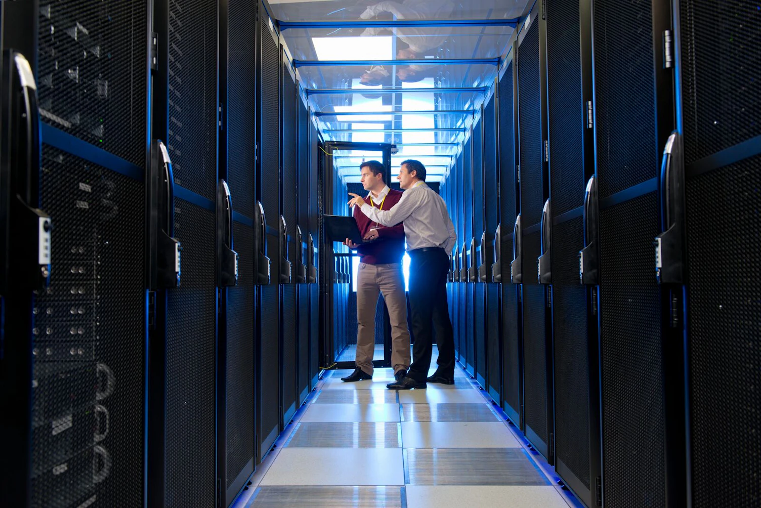 manager and technician with laptop talking in aisle of server room
