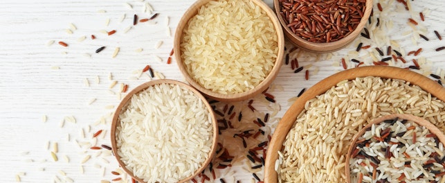 Flat lay composition with brown and other types of rice in bowls on white wooden background
