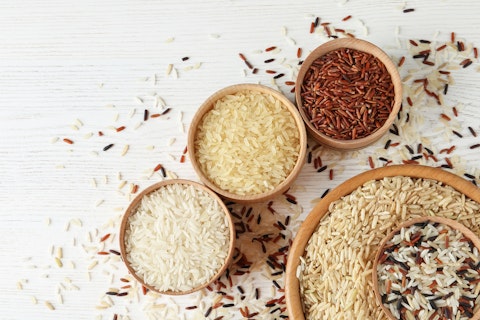 Flat lay composition with brown and other types of rice in bowls on white wooden background