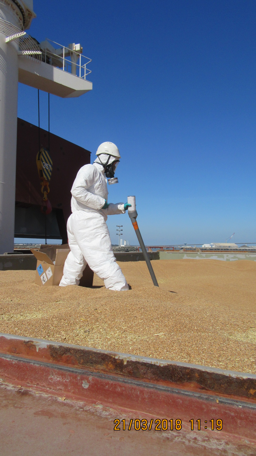 Technicien en combinaison de protection effectuant une fumigation sur une cargaison de grains à ciel ouvert.