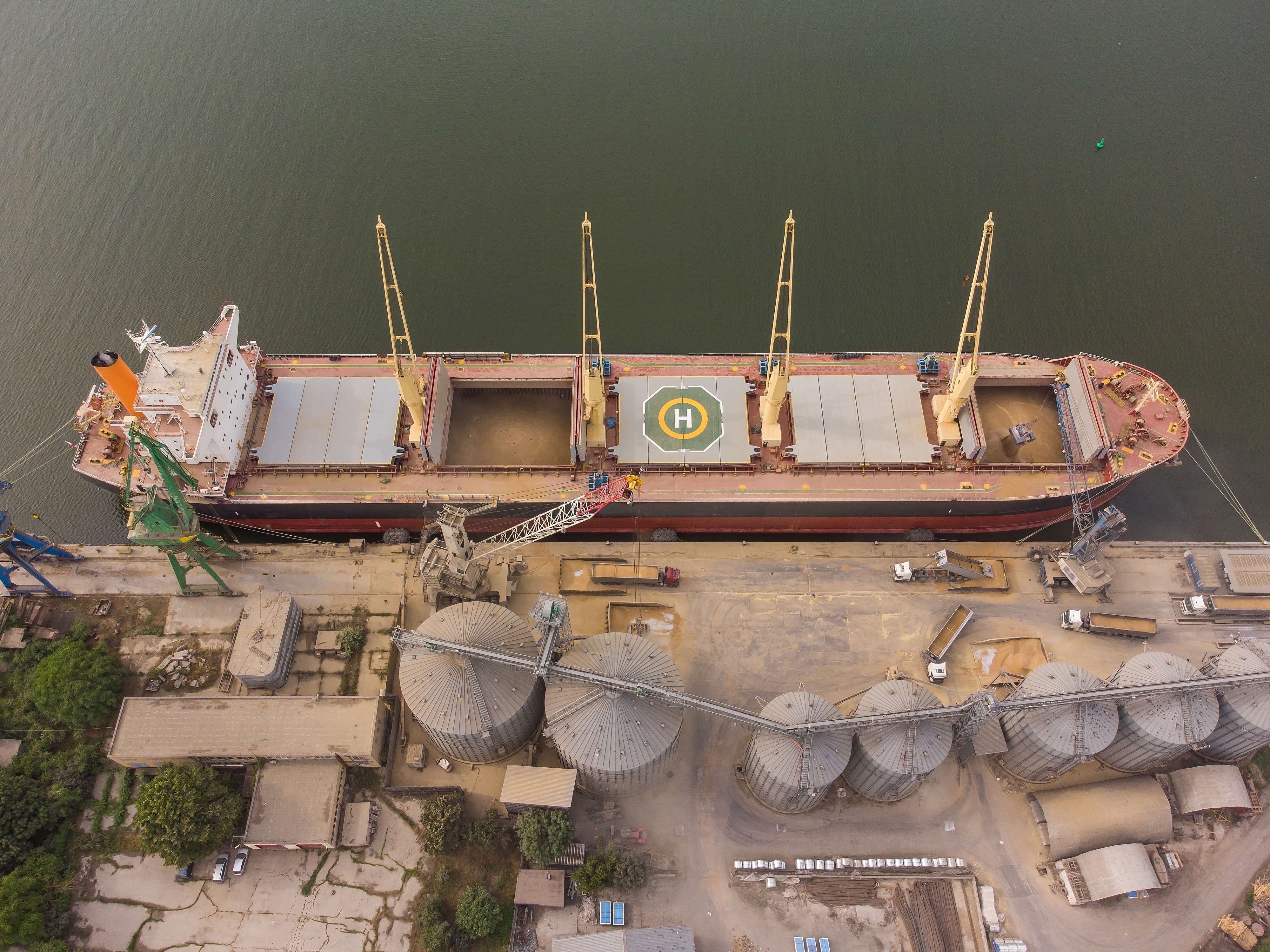 Loading grain into holds of sea cargo vessel in seaport from silos of grain storage. Bunkering of dry cargo ship with grain. Aerial top view